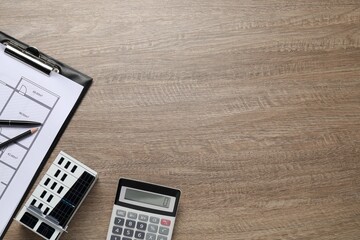 Real estate. Apartment building model, floor plan and calculator on wooden table, flat lay. Space...