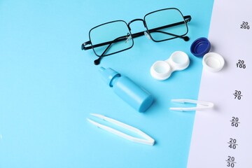 Vision test chart, glasses, tweezers, lenses and bottle of medical drops on light blue background,...