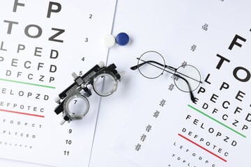 Vision test charts, glasses, trial frame and lenses on white background, flat lay