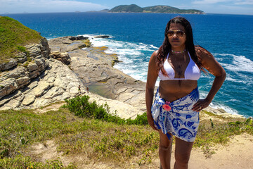 Woman at the viewpoint of Praia das Conhas, lots of rocks and blue waters and mountains in the background. Rio de Janeiro, Brazil.