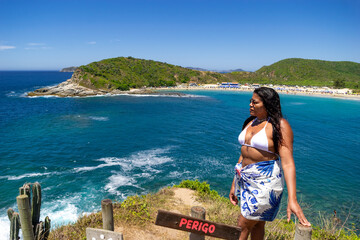 Woman at the viewpoint of Praia das Conhas, with crystal clear waters in the background, mountains and vegetation around. Rio de Janeiro, Brazil.