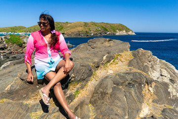 Woman enjoying the view from above the fort of Praia do Forte, many rocks, sky with clouds.