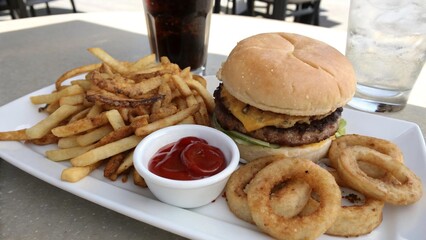 A delicious burger, fries, onion rings, and drinks on a white plate.
