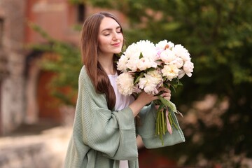 Charming woman with bouquet of beautiful peonies on city street