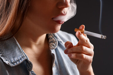 Woman in shirt smoking cigarette on dark background, closeup. Bad habit