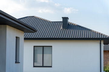A contemporary house features a well-defined roof, a dark chimney, and large windows under a clear...