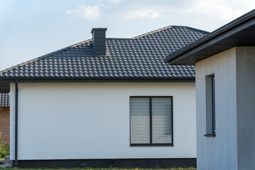 A contemporary white house displays a stylish roof and large window, surrounded by green grass and sky, showcasing a peaceful suburban atmosphere