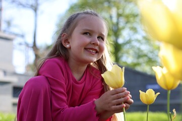 Cute little girl near beautiful yellow tulips outdoors