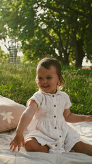Little girl playing with a large straw hat while sitting on a blanket in the park. Soft focus.  Close-Up