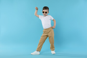 Happy little boy in sunglasses dancing on light blue background