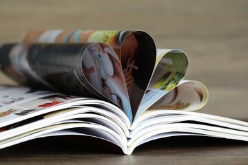 Different open magazines on wooden table, closeup