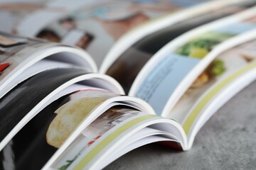 Different open magazines on grey table, closeup