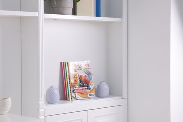 Many different trendy magazines and vases in white shelving unit indoors