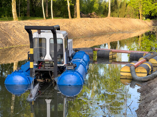 A specialized cleaning machine works in a shallow waterway, removing debris and maintaining the...