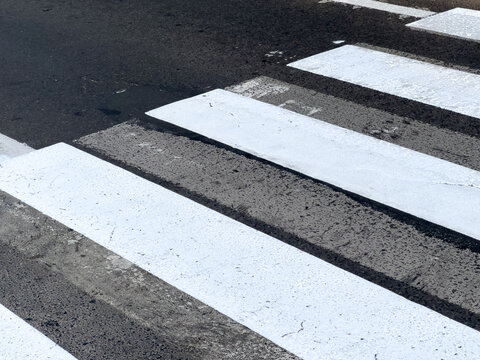 Freshly painted pedestrian crossing lines create a clear path for walkers in a lively urban setting during daylight hours