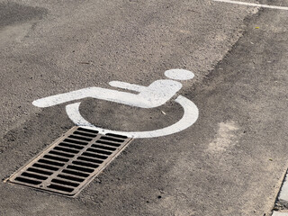 A parking space marked with a disability symbol is positioned directly above a drain in a public...