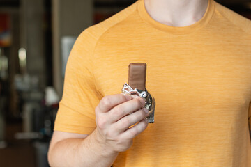 Sporty man eating energy bar. Muscular athlete snacks protein bar while resting after workout at...