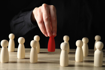 Dismissal. Woman choosing red figure among wooden ones at table, closeup