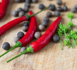 several fresh red chili peppers on a wooden surface surrounded by aromatic peppercorns