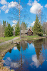 Fototapeta premium Serene Wooden Cabin Beside a Reflective Pond Surrounded by Lush Trees Under a Blue Sky