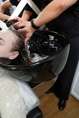 Close-up of hands washing hair in a black sink, showing wet strands after a hair treatment procedure. Professional salon hair care scene highlighting cleanliness and care.