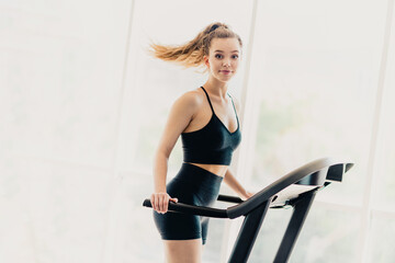 Young woman exercising on a treadmill indoors in sportswear, promoting healthy lifestyle, fitness,...
