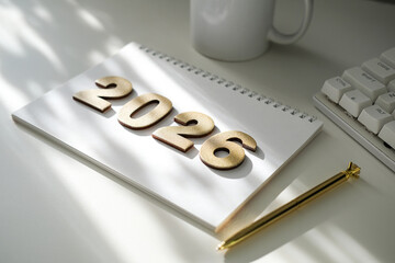 Golden numbers 2026 on notebook, golden pen, white mug and keyboard part, bathed in soft sunlight. Planning, goals, new beginnings. Ideal for business, education