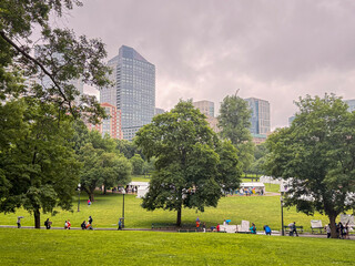 Urban park with trees and skyscrapers under cloudy sky