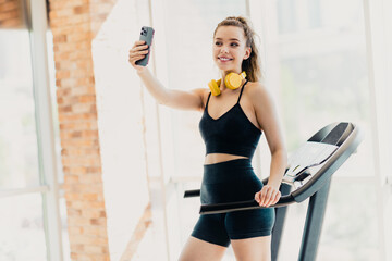 Active woman in activewear taking a selfie on a treadmill during her cardio workout in a...