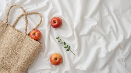 Bohemian style wicker bag and ripe red apples with green leaves on white linen background, cosmetic or jewelry accessory product placement and copy text space