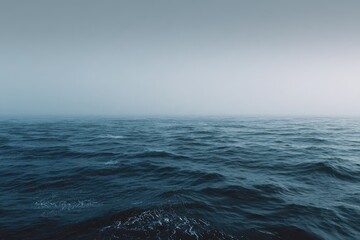 A tranquil, hazy ocean scene at dawn or dusk, with dark blue water and a muted sky, showing gentle waves and a calm, vast expanse