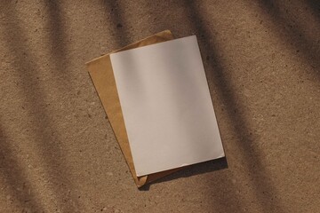 Blank paper greeting card, invitation. Craft envelope, textured concrete stone background. Natural sunlight, shadows. Minimal composition. Wedding stationery mockup, branding design. Flat lay, top