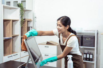 Young housekeeper wearing gloves and cleaning the table with a rag and cleaning spray. Professional...