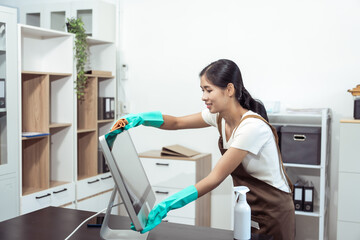 Young housekeeper wearing gloves and cleaning the table with a rag and cleaning spray. Professional...