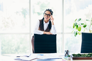 Successful businesswoman smiling confidently in a modern office workspace surrounded by...