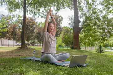Young woman with closed eyes lifting arms overhead in a yoga stretch while seated cross-legged on...