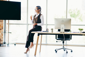 Confident businesswoman in formal attire enjoying a coffee break at a bright and modern office...