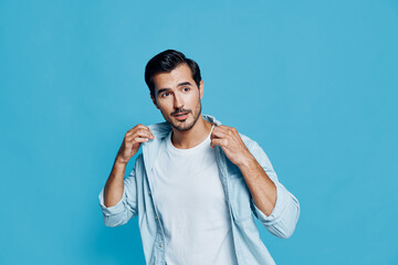 Fototapeta premium Handsome young man in light denim shirt pulling collar, looking at the camera with a thoughtful expression against a vibrant blue background. Style and confidence concept.