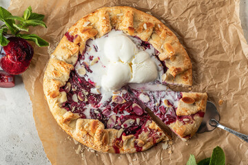Sliced galette or pie with plums and almonds served with ice cream scoops on parchment paper...