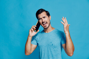 Energetic man talking on smartphone with raised hand, expressing frustration or excitement, wearing...