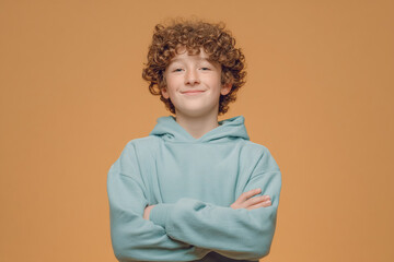Boy with arms crossed in blue hoodie smiles confidently.