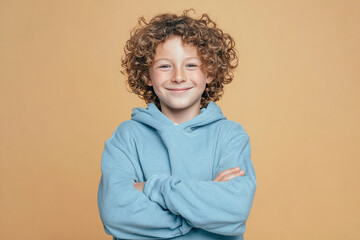 Smiling boy stands with arms crossed against beige background. Perfect for marketing, advertising, web use.