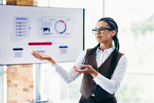 Successful businesswoman presenting analytics and strategy solutions in an office with a screen displaying visual data charts