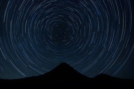 A dramatic long-exposure photograph captures star trails swirling in concentric circles over a silhouetted mountain peak at night