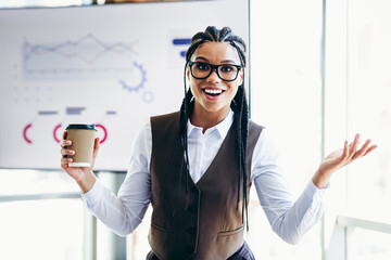 Confident businesswoman presenting with a drink in a professional office environment with charts...