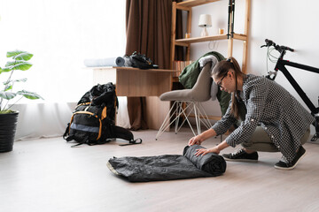 Female Backpacker in eyeglasses rolling sleeping bag for camping, packing for her trip at home...
