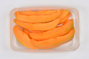 A clear plastic container is filled with several vibrant orange cantaloupe slices, neatly arranged...