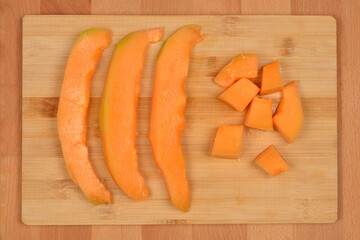Three long slices and several cubed pieces of vibrant orange cantaloupe are arranged on a light...