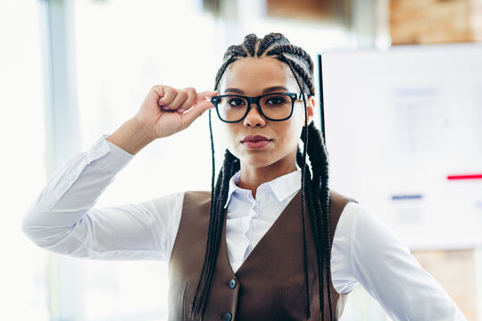 Professional professional woman in business attire posing confidently in office environment with stylish braids and glasses