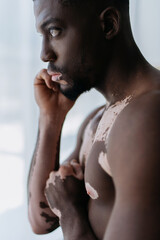 Side view of shirtless african american man with vitiligo standing at home